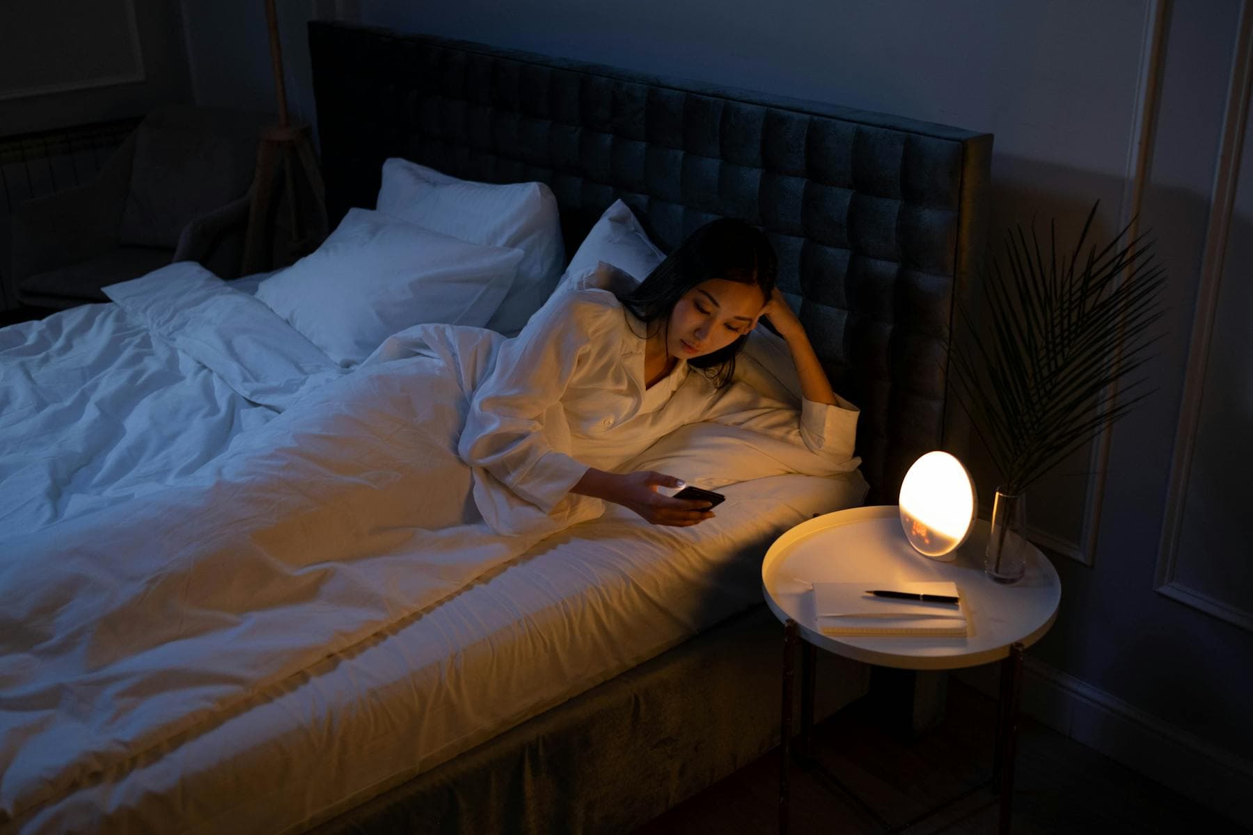 Tired woman lying awake in a dim bedroom at night, illustrating the cumulative science of sleep debt and why one good night cannot repay it.