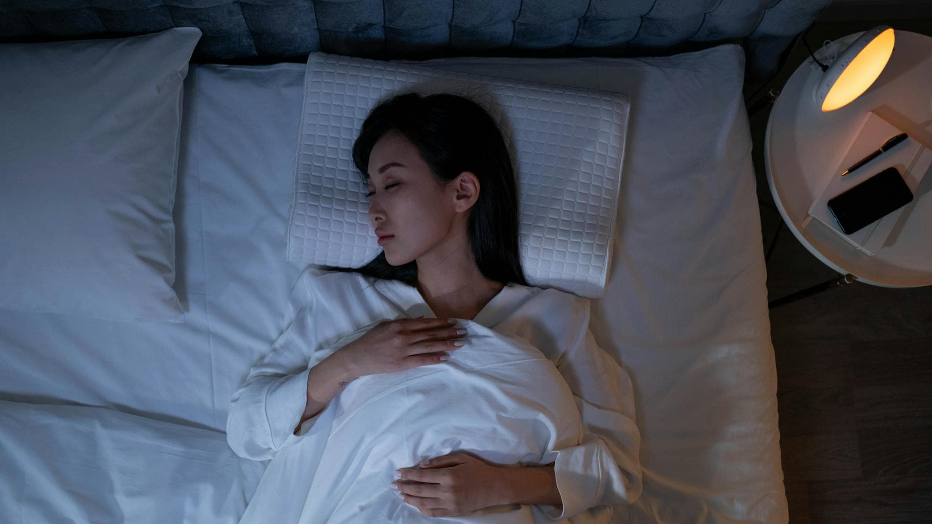 Woman sleeping peacefully in a dimly lit bedroom, illustrating restorative deep sleep for brain and body recovery