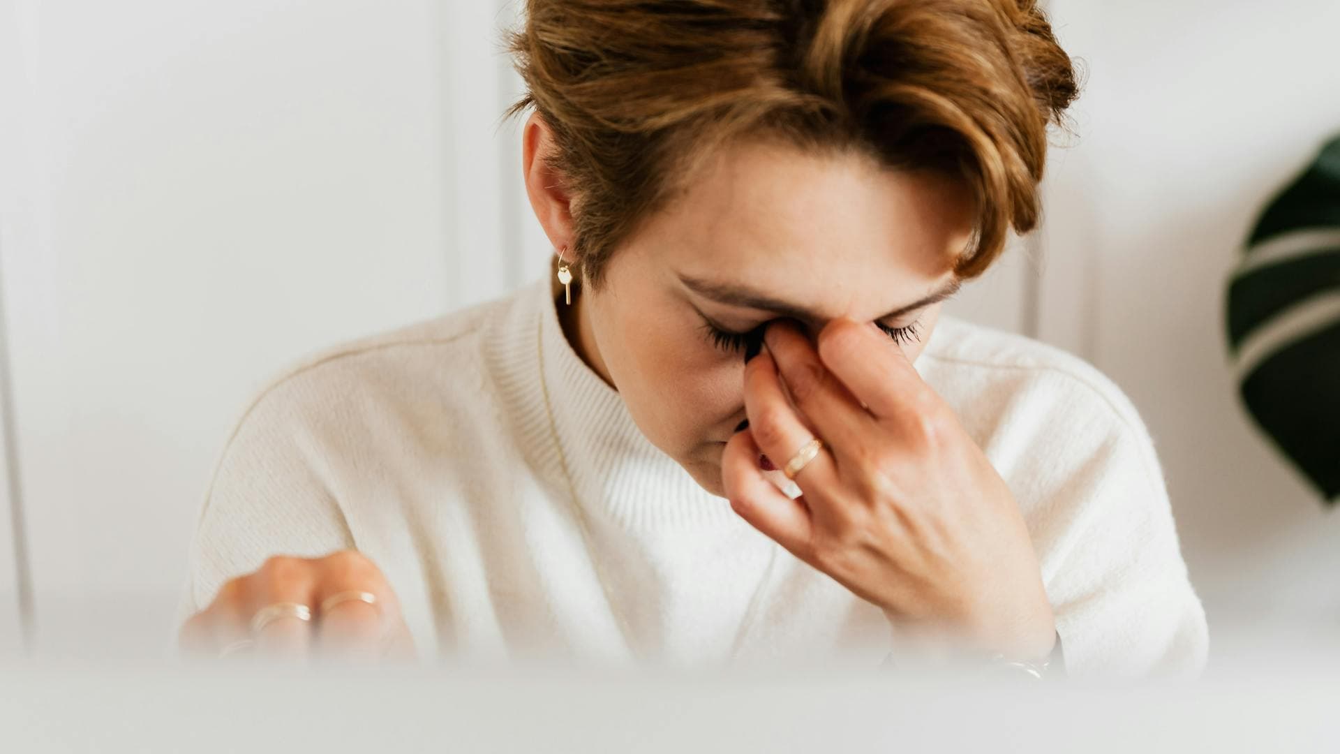 Close-up of a woman rubbing her eyes in fatigue, conveying the physical toll of chronic stress and sleep deprivation on the body — from Nghê Prana, a Hoi An riverside hotel and wellness spa