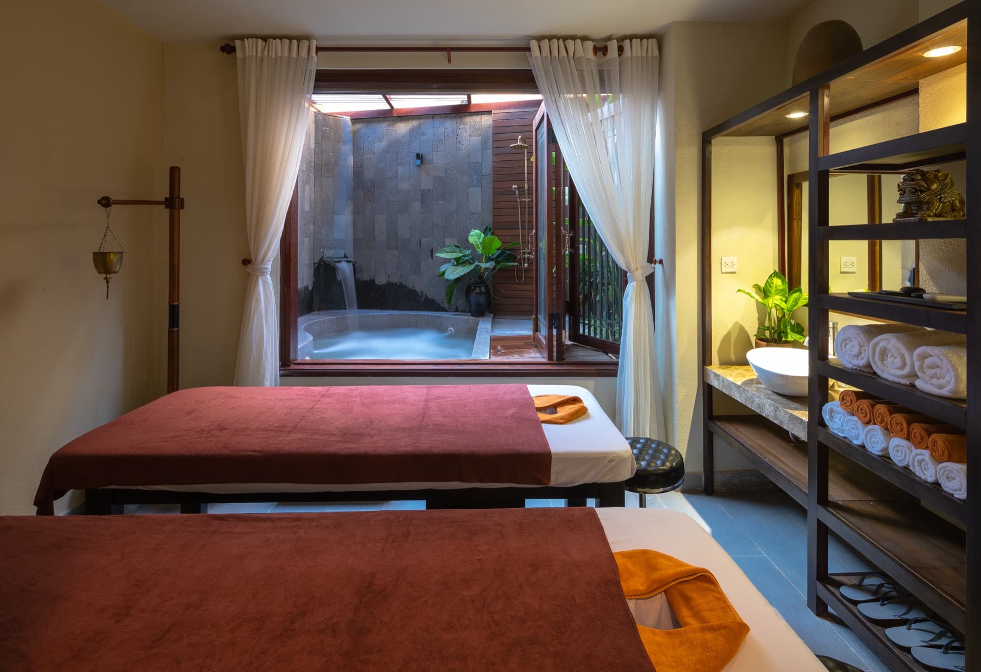 Twin massage beds facing the private jacuzzi in the couples treatment room at Nghê Prana, a Hoi An riverside hotel and Vietnamese herbal spa
