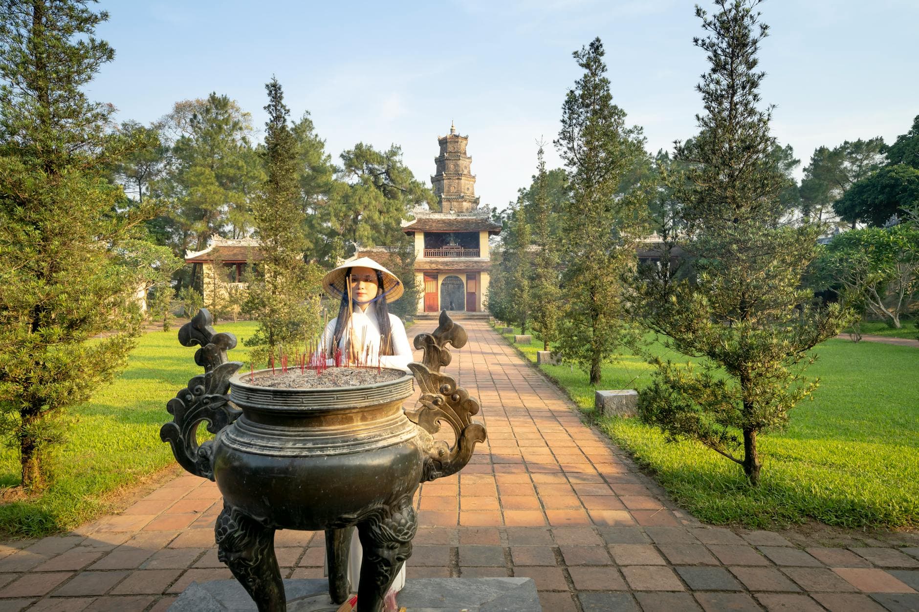 Three lit incense sticks held in joined palms before a Vietnamese pagoda altar — the basic offering gesture (chắp tay khấn) used by laypeople during Phật Đản pagoda visits.