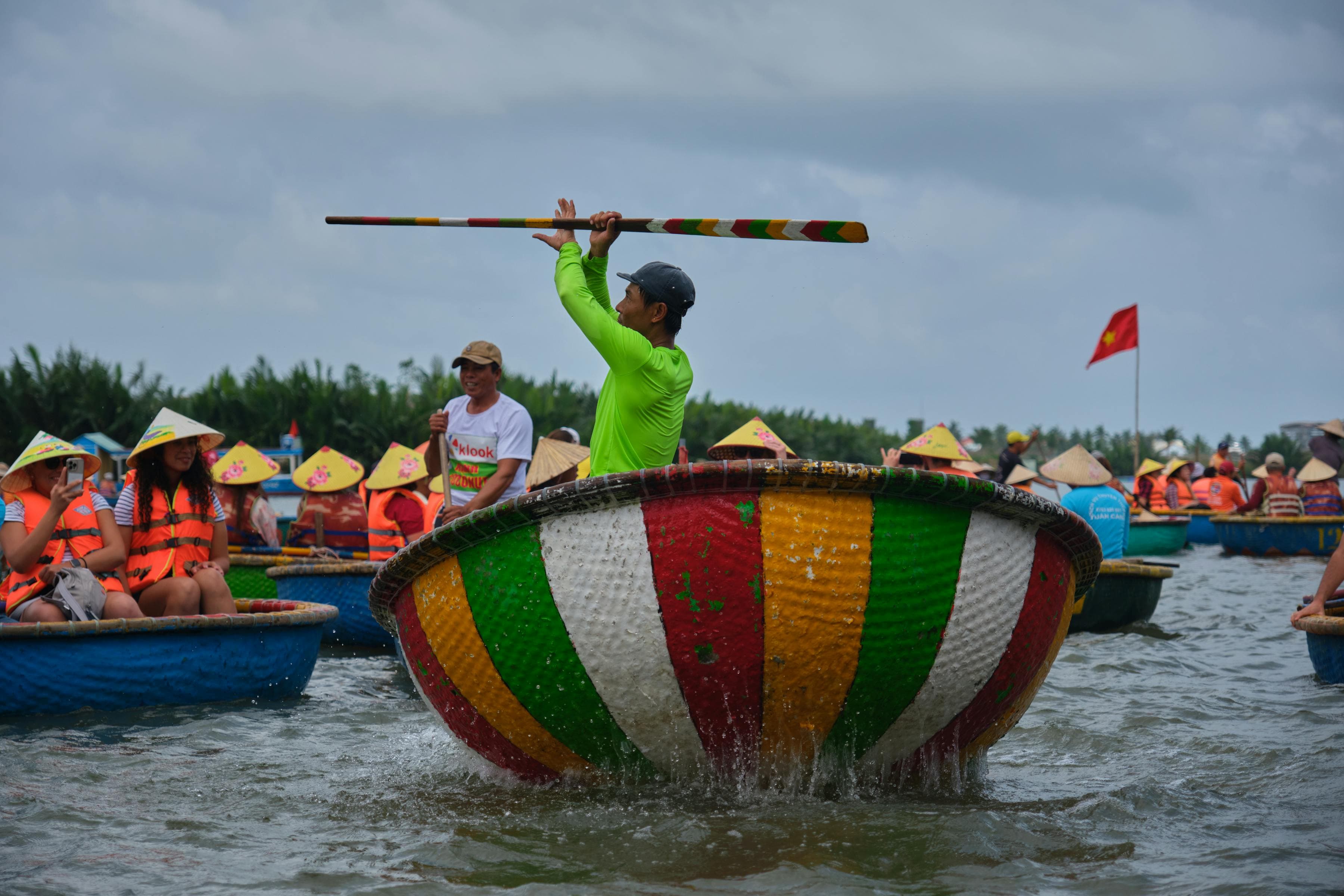 A boatman spinning a round bamboo basket boat (thuyền thúng) in the brackish water at Cẩm Thanh nipa palm coconut village, Hội An, Vietnam — the estuarine village 5 km east of the Ancient Town