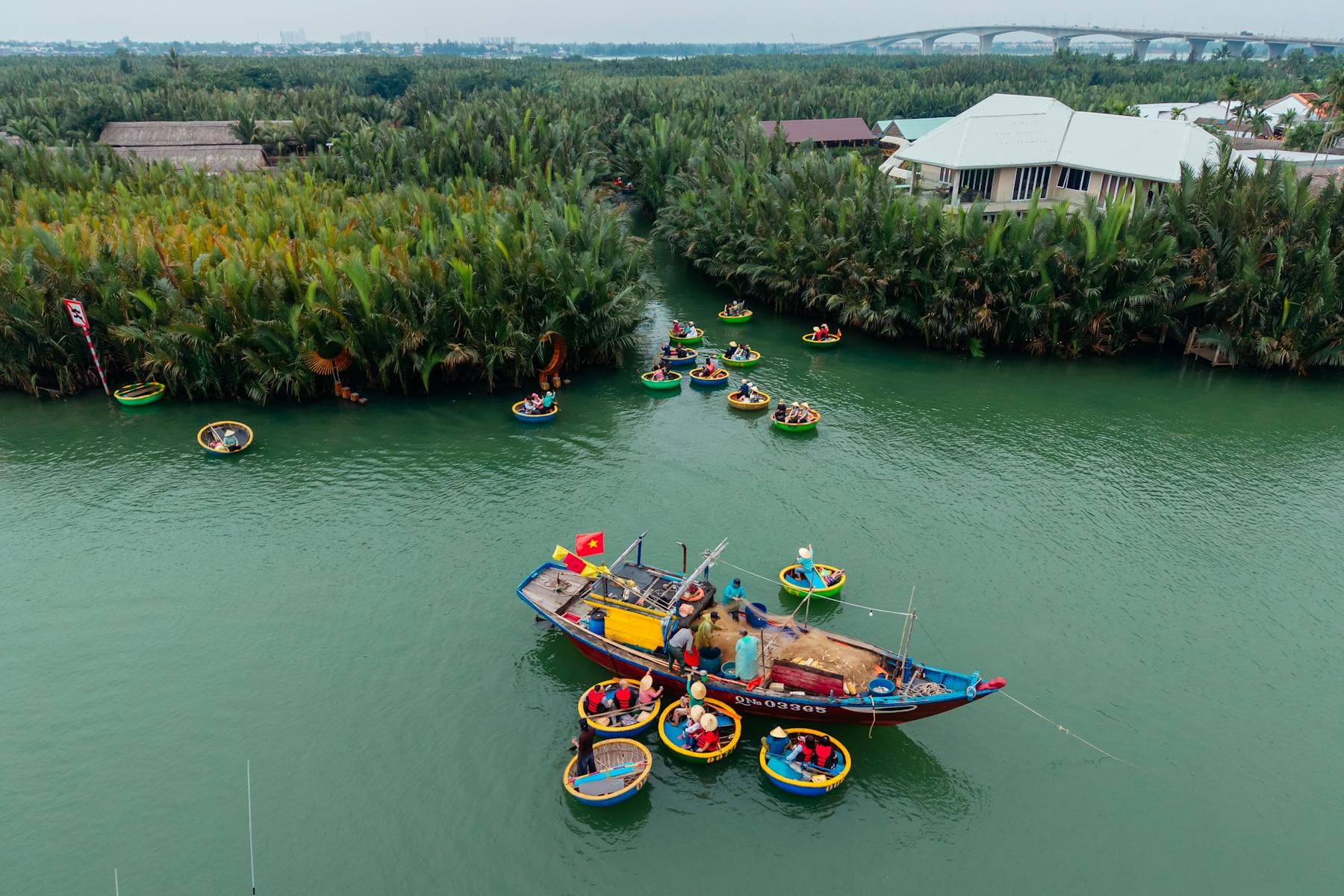 Aerial view of the Cẩm Thanh nipa palm coconut village on the Thu Bồn River estuary, Hội An, Vietnam — traditional thuyền thúng round bamboo basket boats and a wooden fishing boat in the green brackish water
