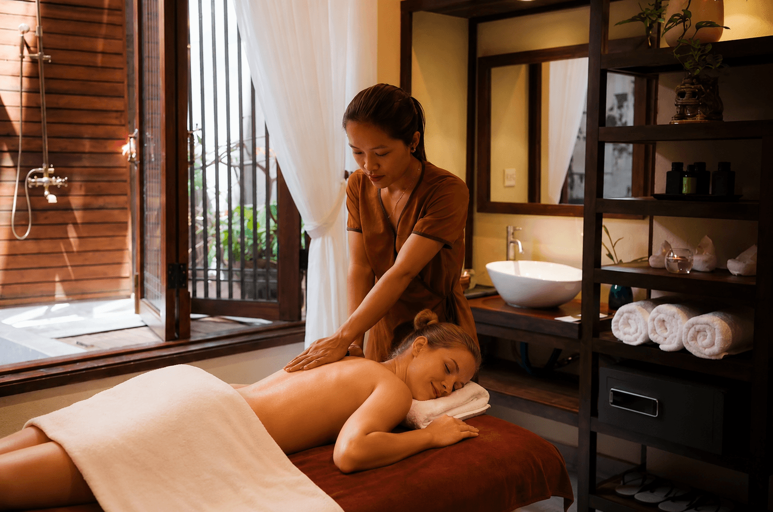 A therapist working on a guest's back in a wood-lined treatment room at Nghê Prana, a Hoi An riverside hotel and Vietnamese herbal spa