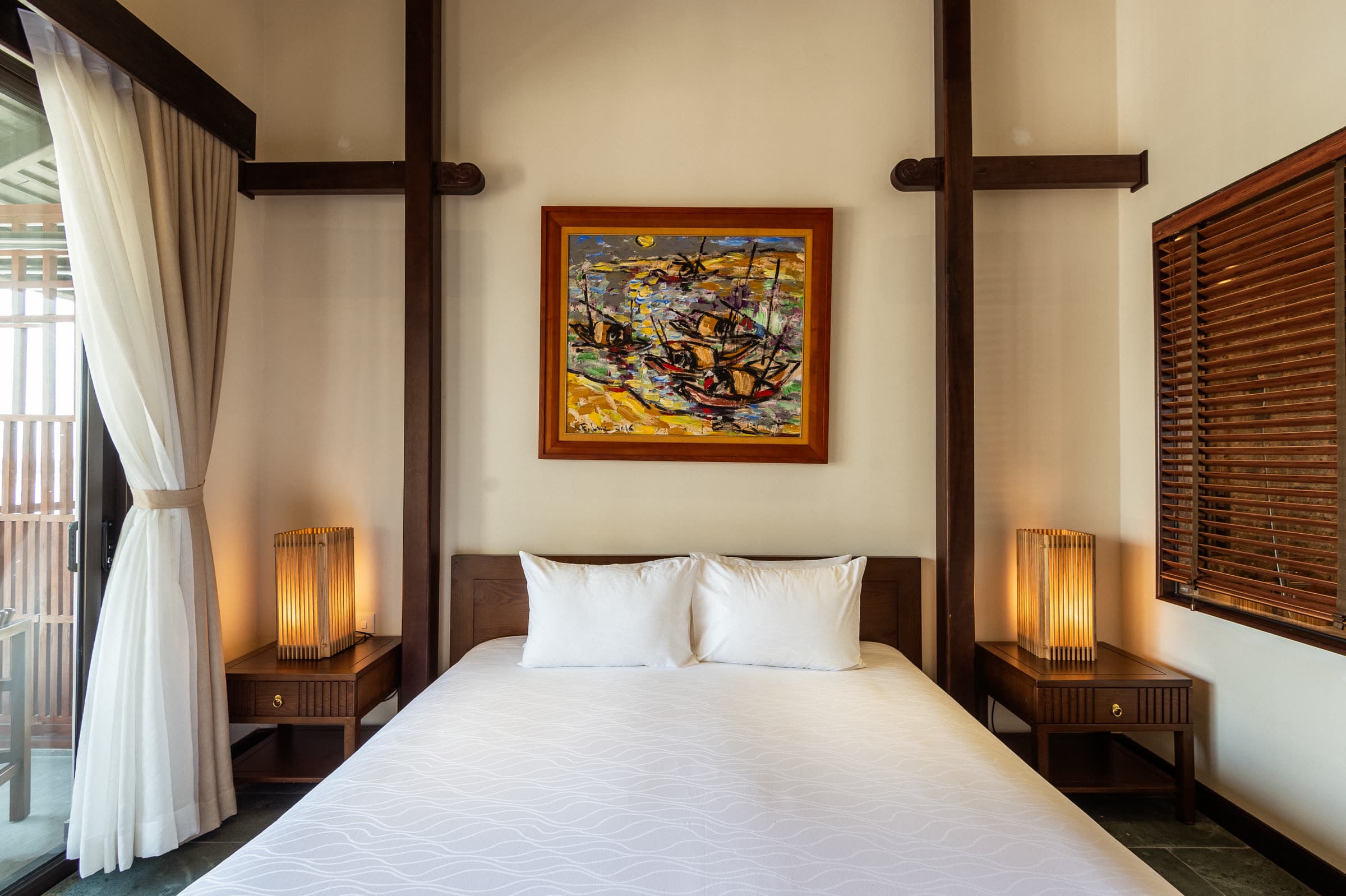 Deluxe Double bed beneath a framed Vietnamese painting, woven lanterns to either side