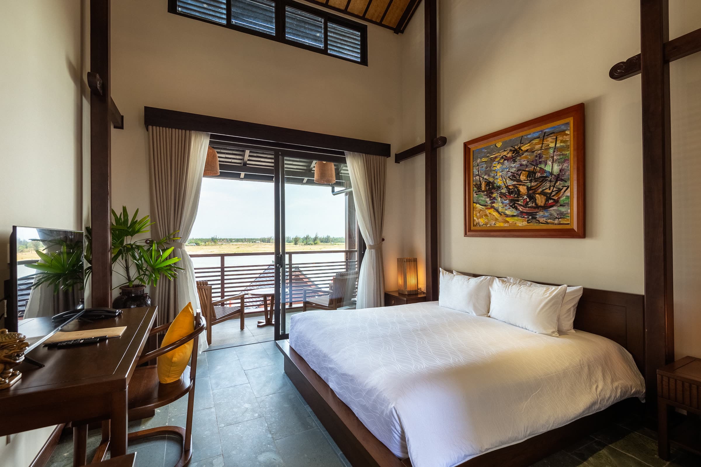 Deluxe Double room with a writing desk and the Thu Bồn River through the balcony doors