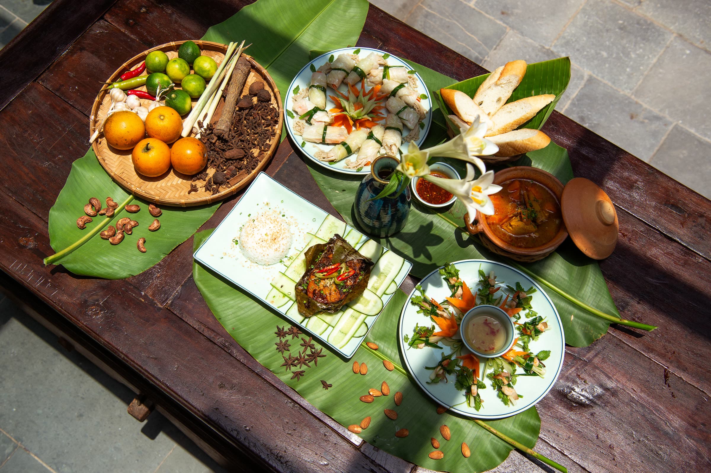 A spread of Vietnamese dishes laid out on banana leaf at Nghê Prana, Hội An — grilled fish, fresh herbs, dipping sauces and rice