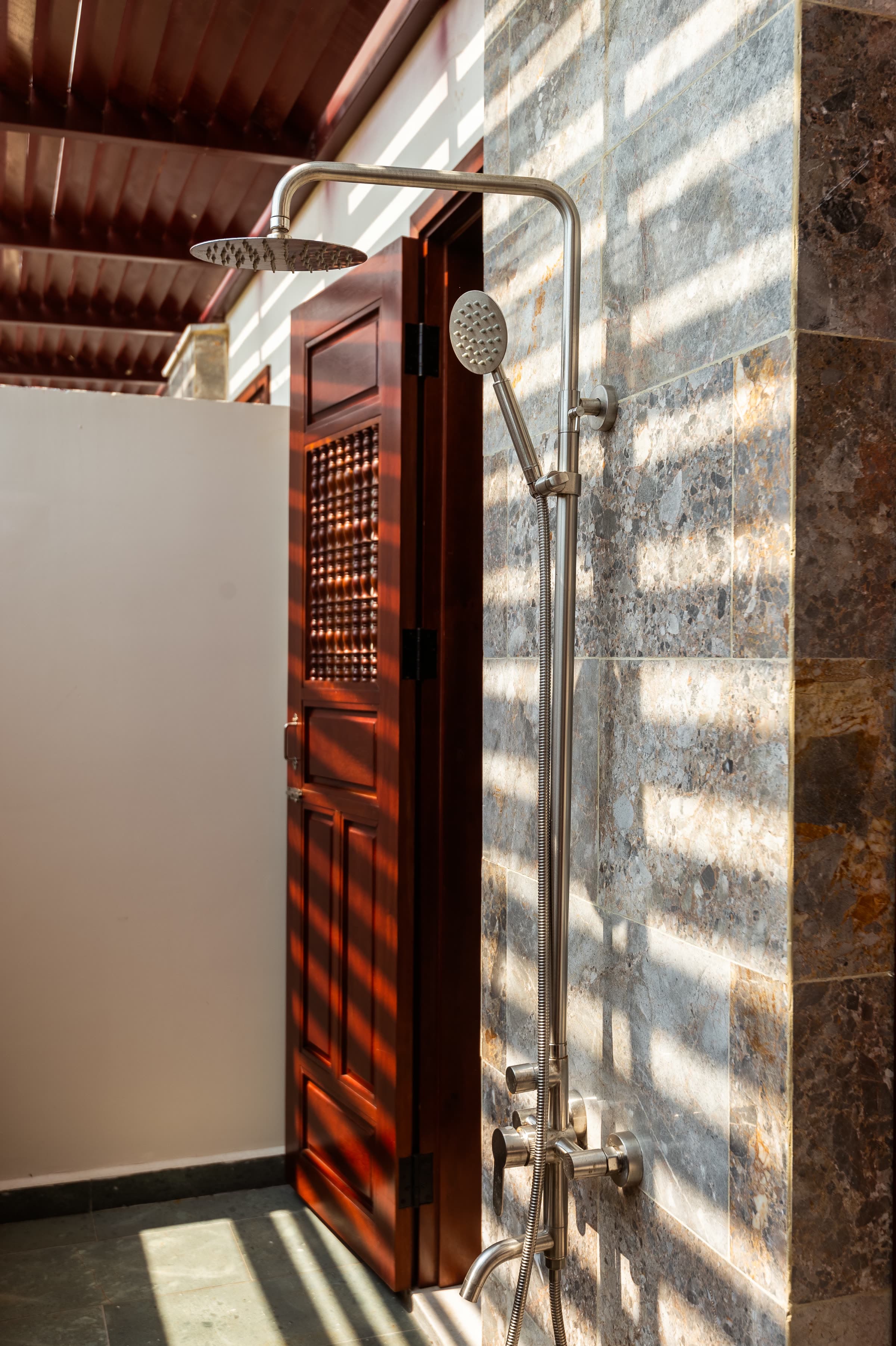 Timber door to the Junior Suite's outdoor shower, sunlight striping the stone wall