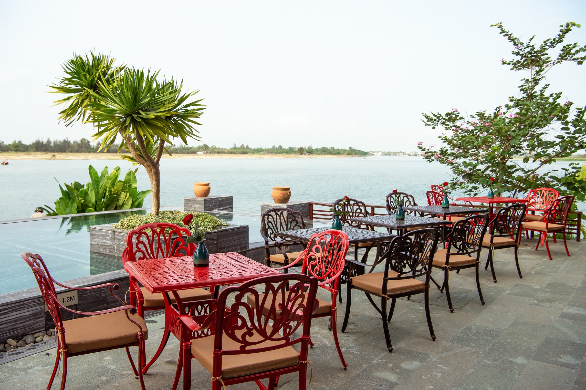 Tables set for breakfast on the riverside terrace at Nghê Prana, the Thu Bồn River just beyond the edge of the pool