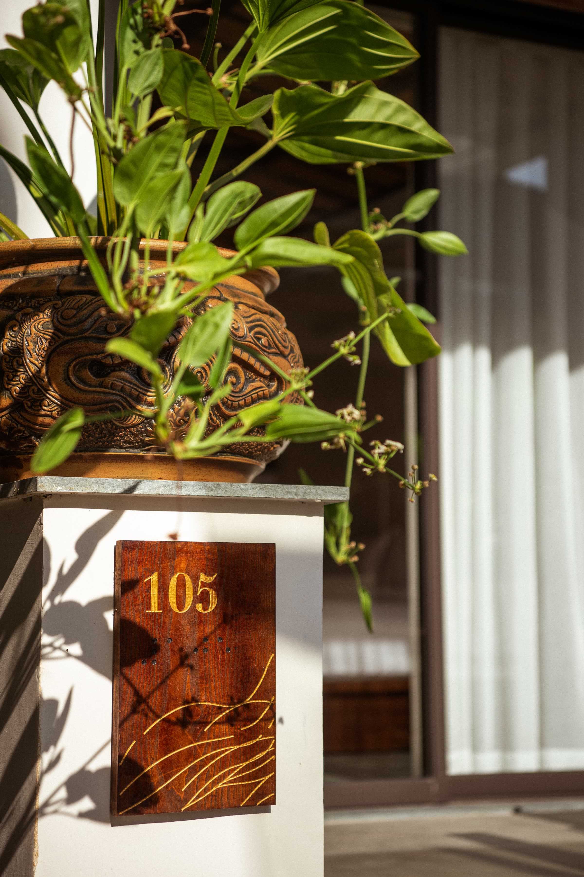The brass-on-timber room number plaque outside a guest room at Nghê Prana, Hội An