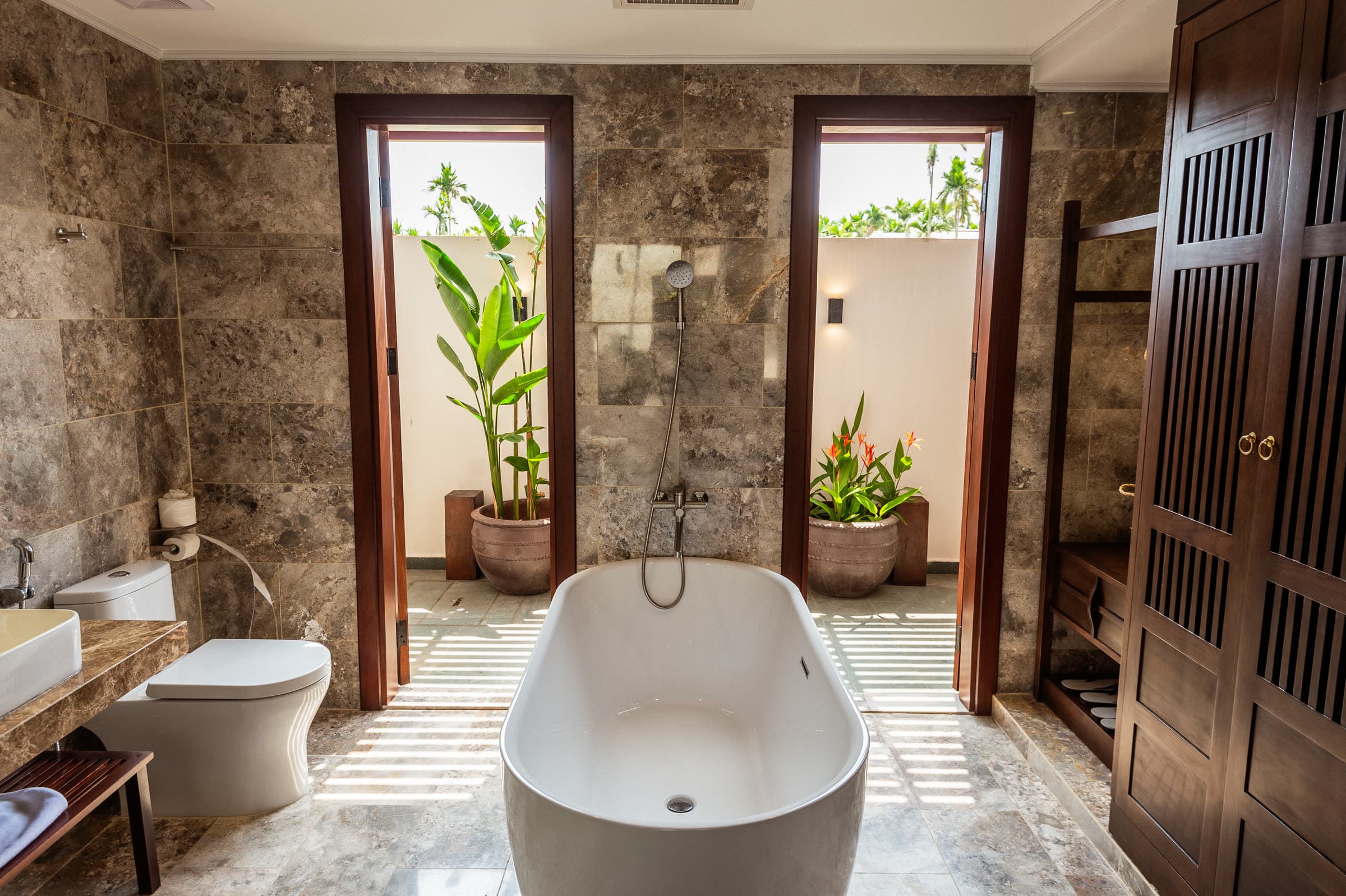 Freestanding white bathtub in the stone bathroom of the Junior Suite, opening onto a planted private courtyard