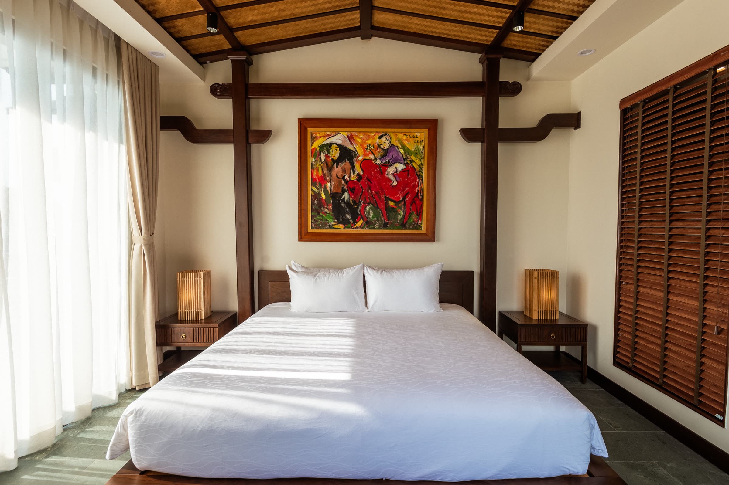 River Suite bed beneath a framed painting, with louvred timber shutters alongside