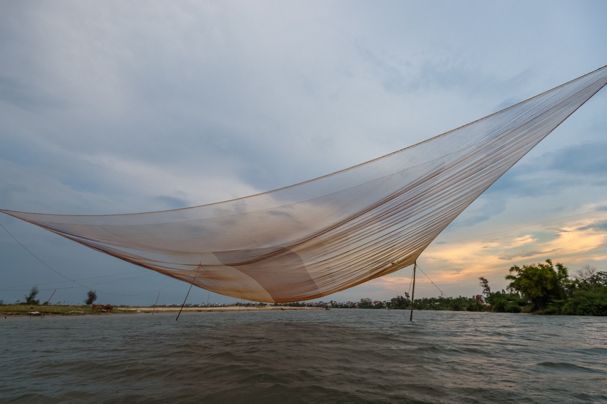 A square dip net standing over the Thu Bồn River at sunset near Hội An