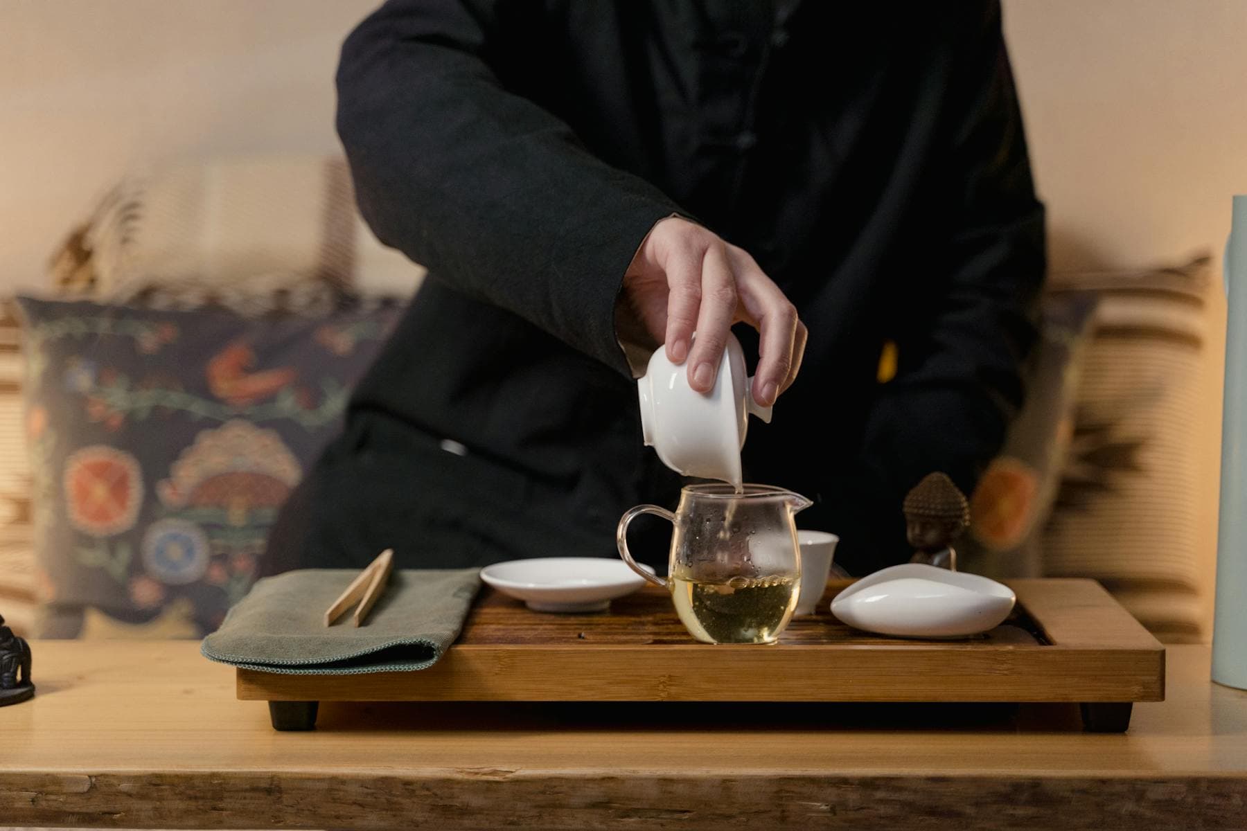 Pouring glass gaiwan teapot wellness tea ritual with small Buddha figure — Chinamaxxing aesthetic experienced in Hoi An Vietnam alternative to China