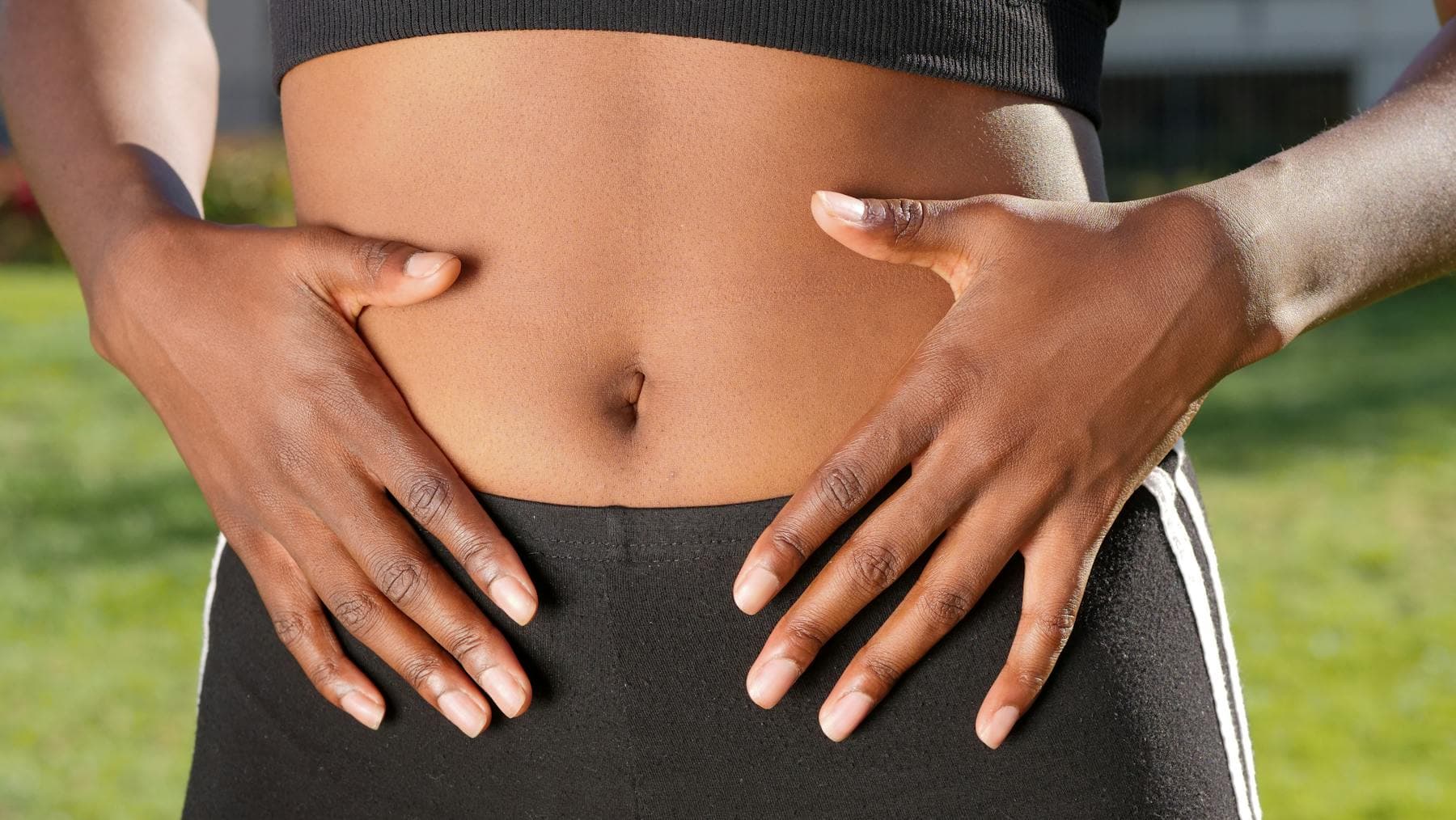 Hands resting on bare midriff illustrating the cortisol belly connection between chronic stress and visible aging.