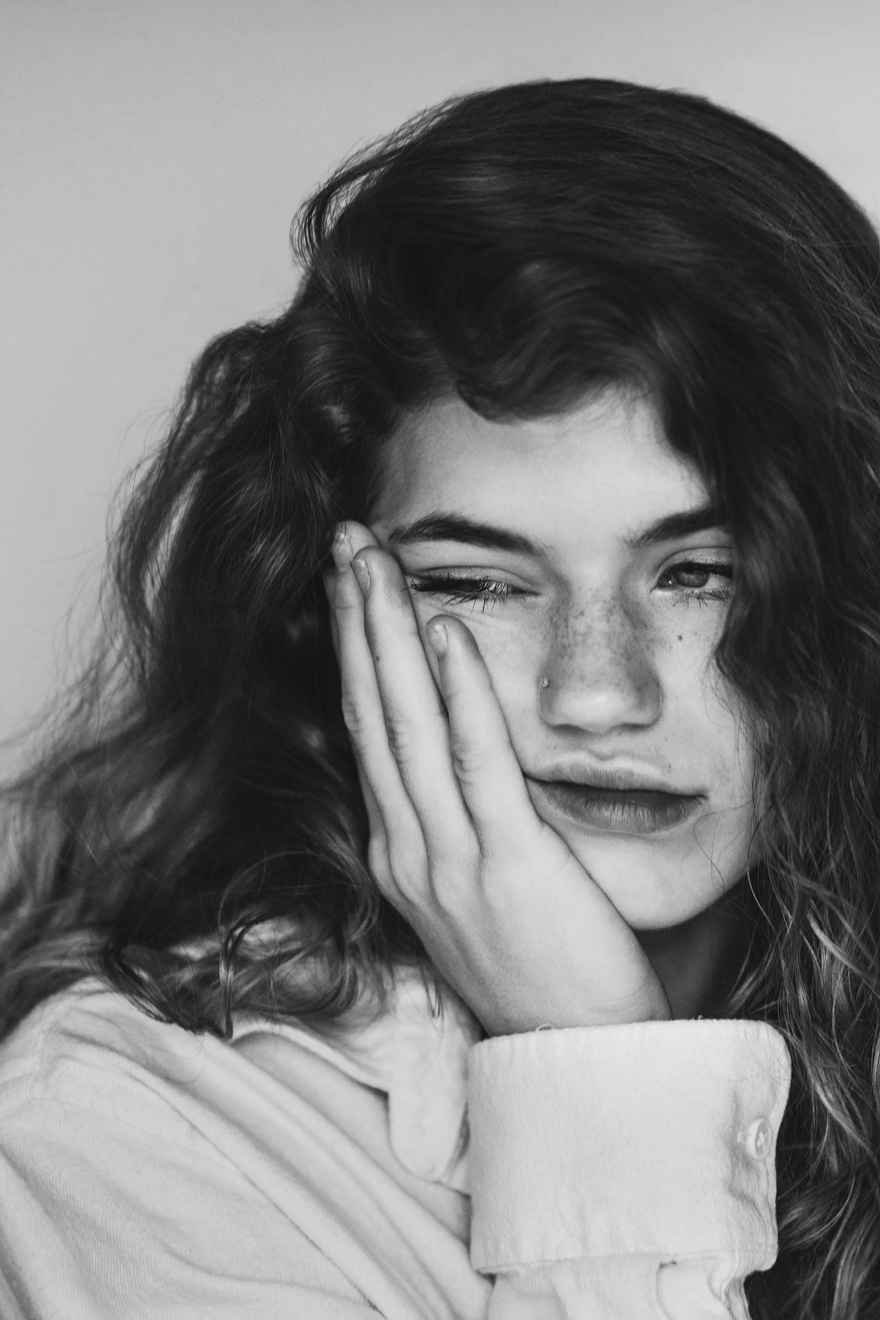 Black and white portrait of a tired woman touching her cheek, illustrating cortisol face — the puffy, stressed facial pattern from chronic high cortisol that a Hoi An riverside sleep retreat can help reverse