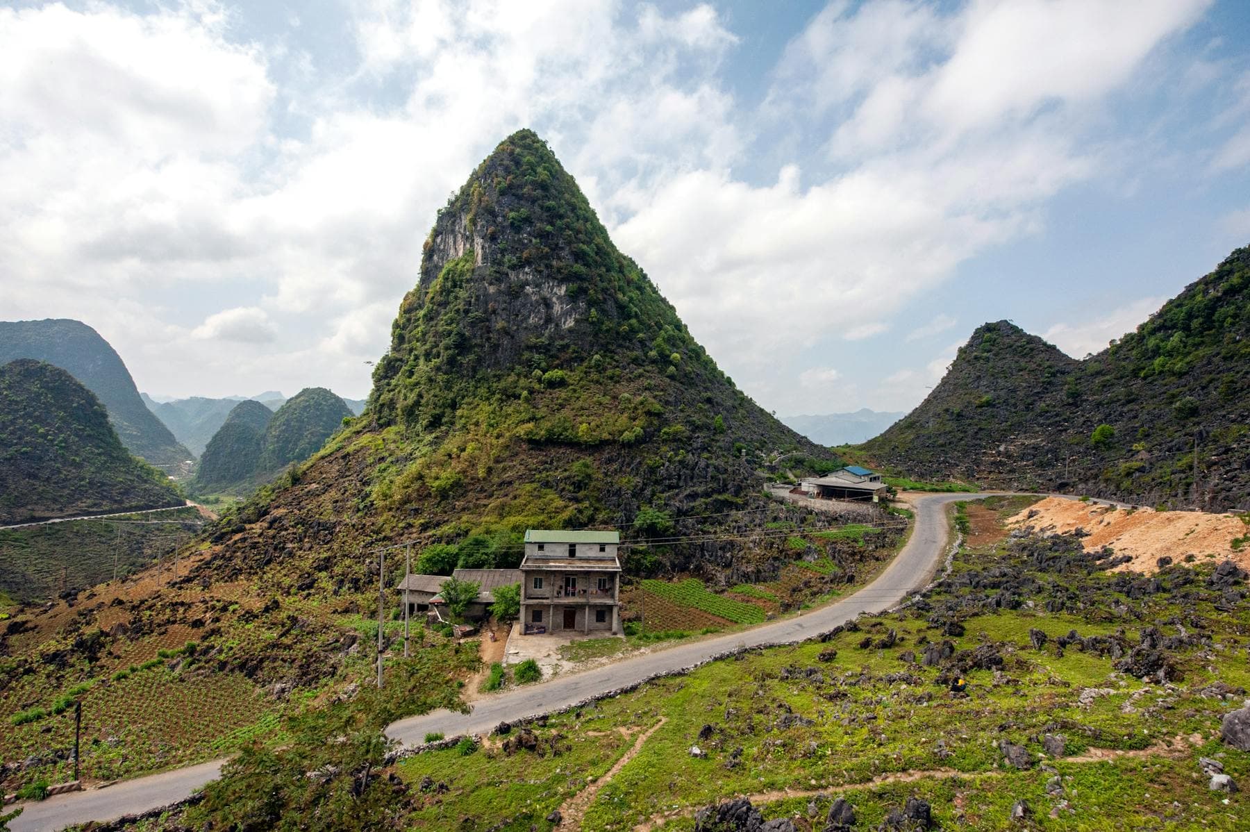 Karst peak rising above a winding mountain road and small village in Hà Giang province, northern Vietnam — the Hà Giang Loop alternative to a slow Hoi An riverside stay in 2026, from Nghê Prana
