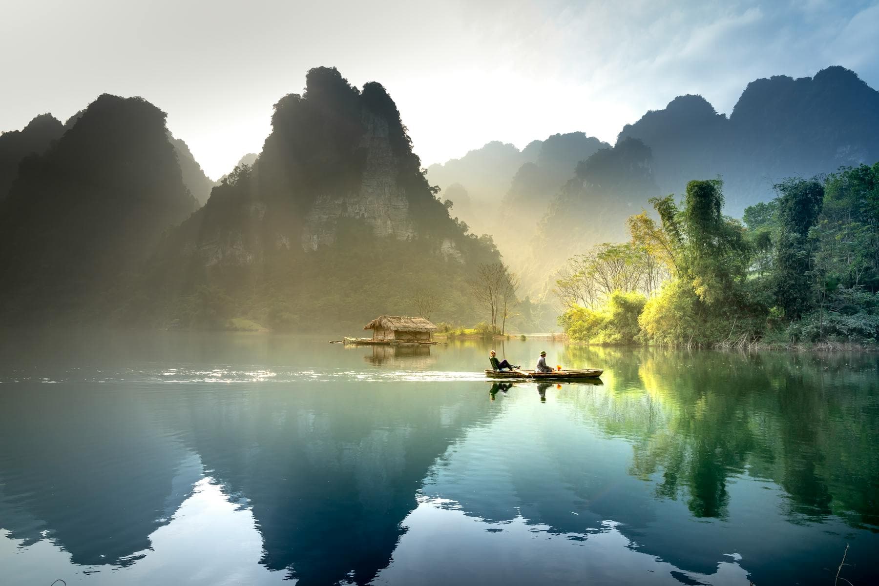 Misty dawn over a quiet Vietnamese river with karst mountains and a small boat — the Hội An quiet side that TikTok does not show