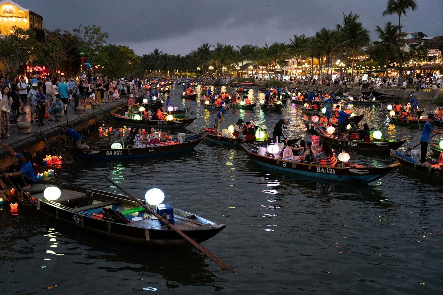 Wooden boats with glowing silk lanterns float on the Thu Bon River during the Hoi An Lantern Festival, the 14th-night full-moon release that runs every lunar month in 2026