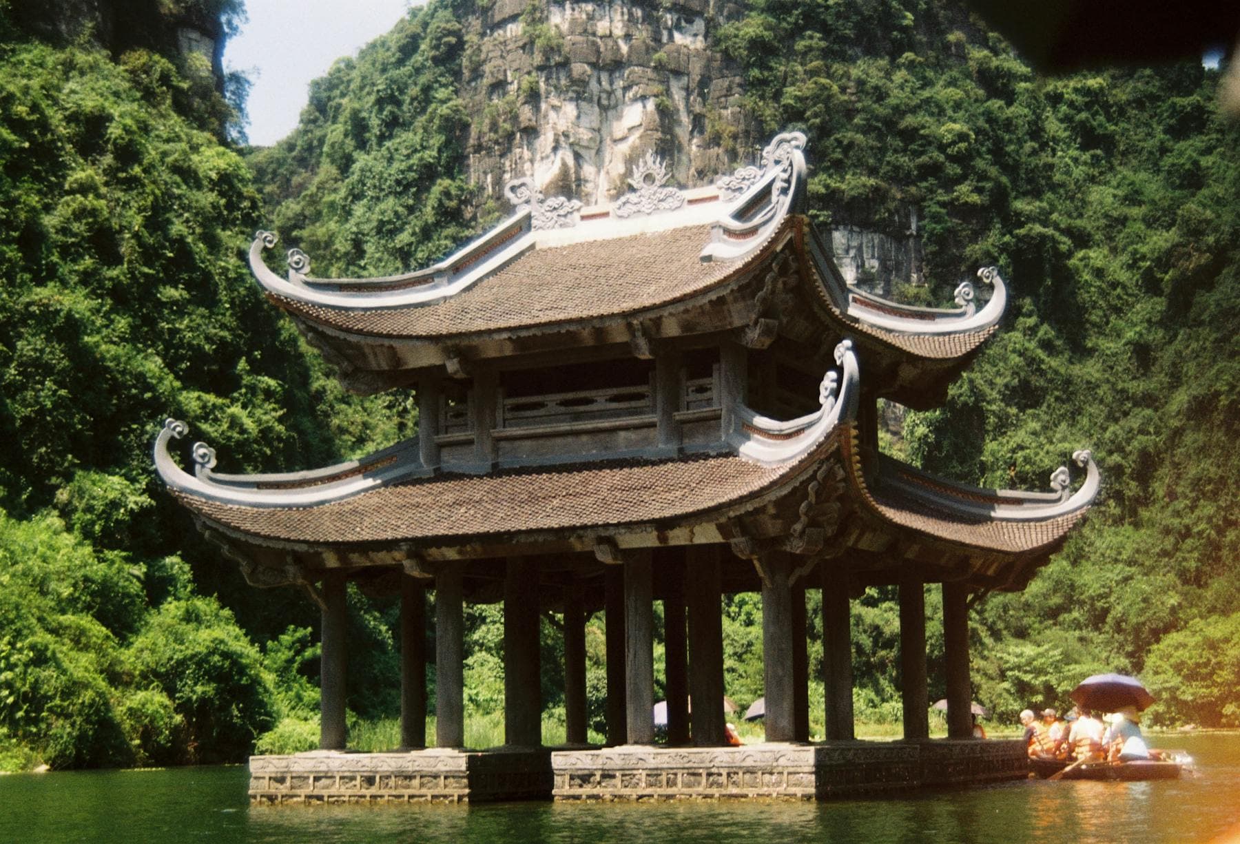 Traditional curved-roof pagoda on the water against limestone karst cliffs at Tràng An, Ninh Bình — wellness retreat comparison with Hoi An riverside, from Nghê Prana, a Hoi An riverside hotel and wellness spa