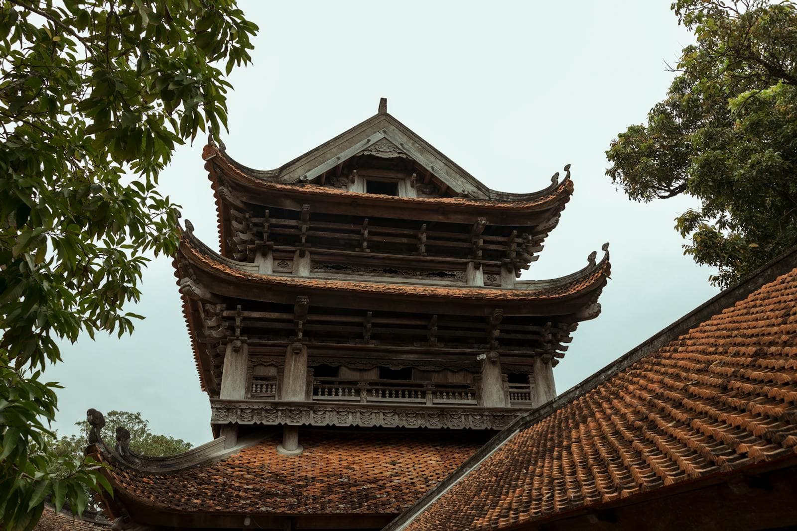 Traditional Vietnamese Buddhist pagoda with curved tile roof and timber gables in soft daylight — the Mahayana architecture seen at Hoi An pagodas during Phat Dan Vesak week.