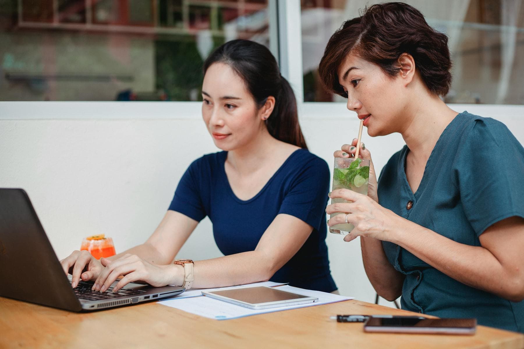 Two Asian women working on a laptop in a cafe with fresh drinks — Hoi An 90 day e-visa digital nomad remote work 2026