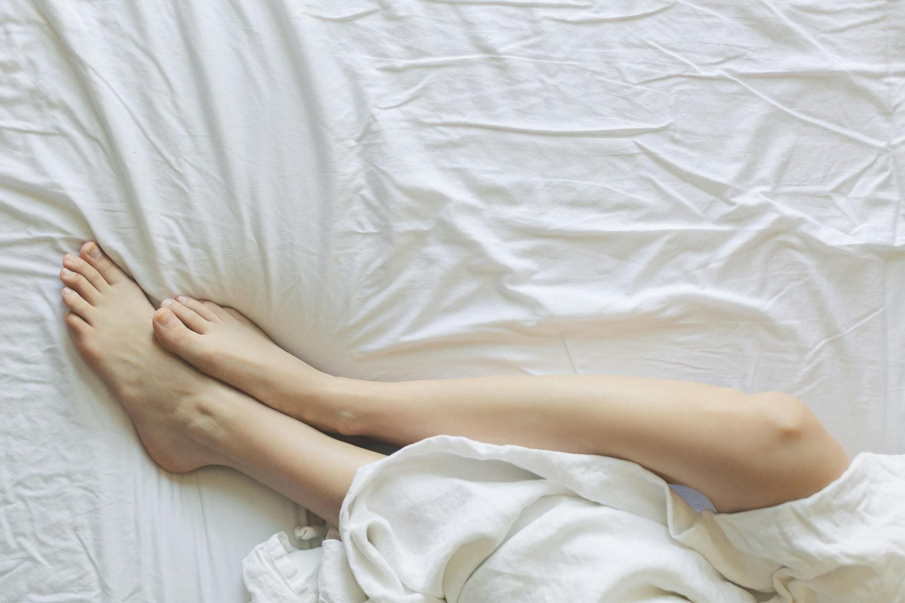 Bare legs resting on white linen sheets representing the complete science of sleep and overnight body and brain restoration.