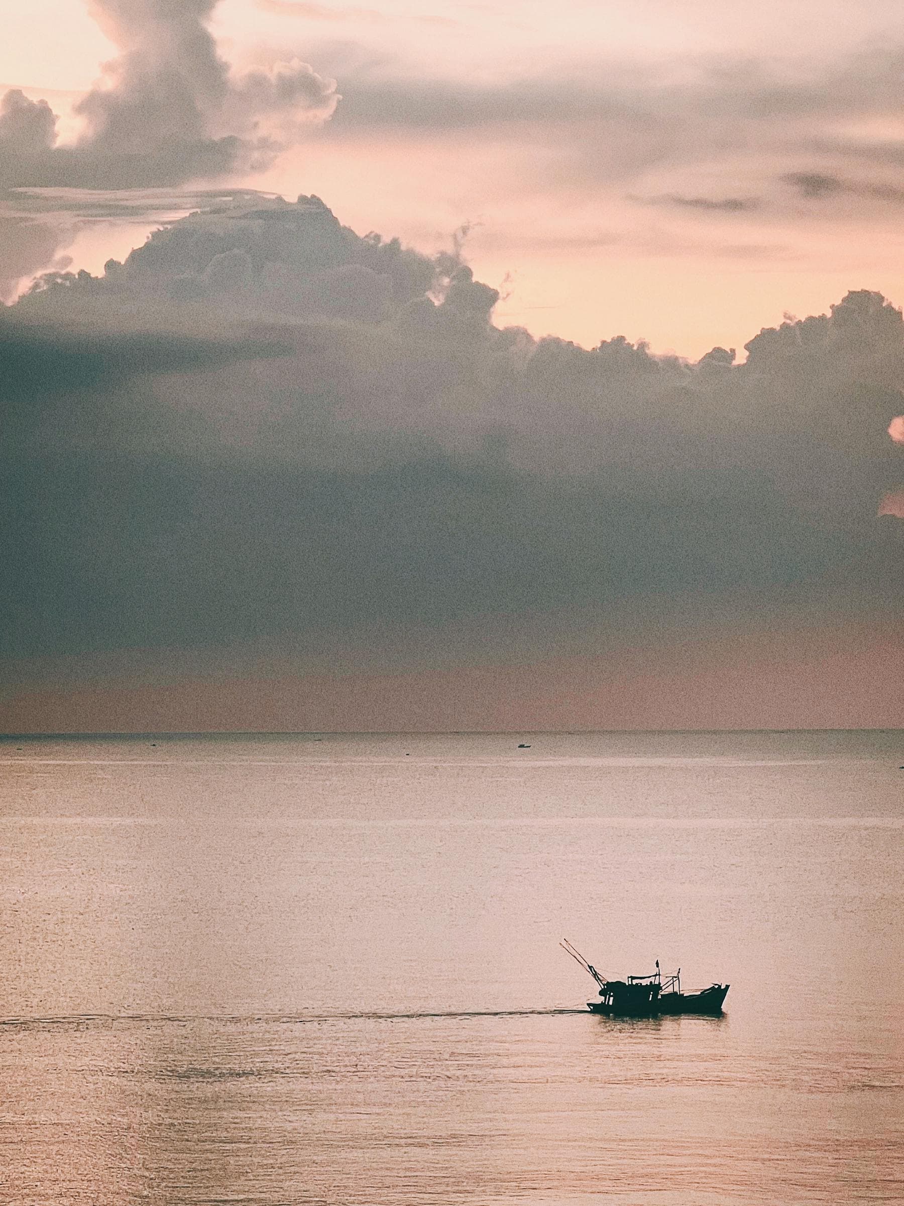 Silhouetted fishing boat on calm water under a pink and grey sunset sky — Thu Bồn River sunset vantage points and the best Hội An sunset spots