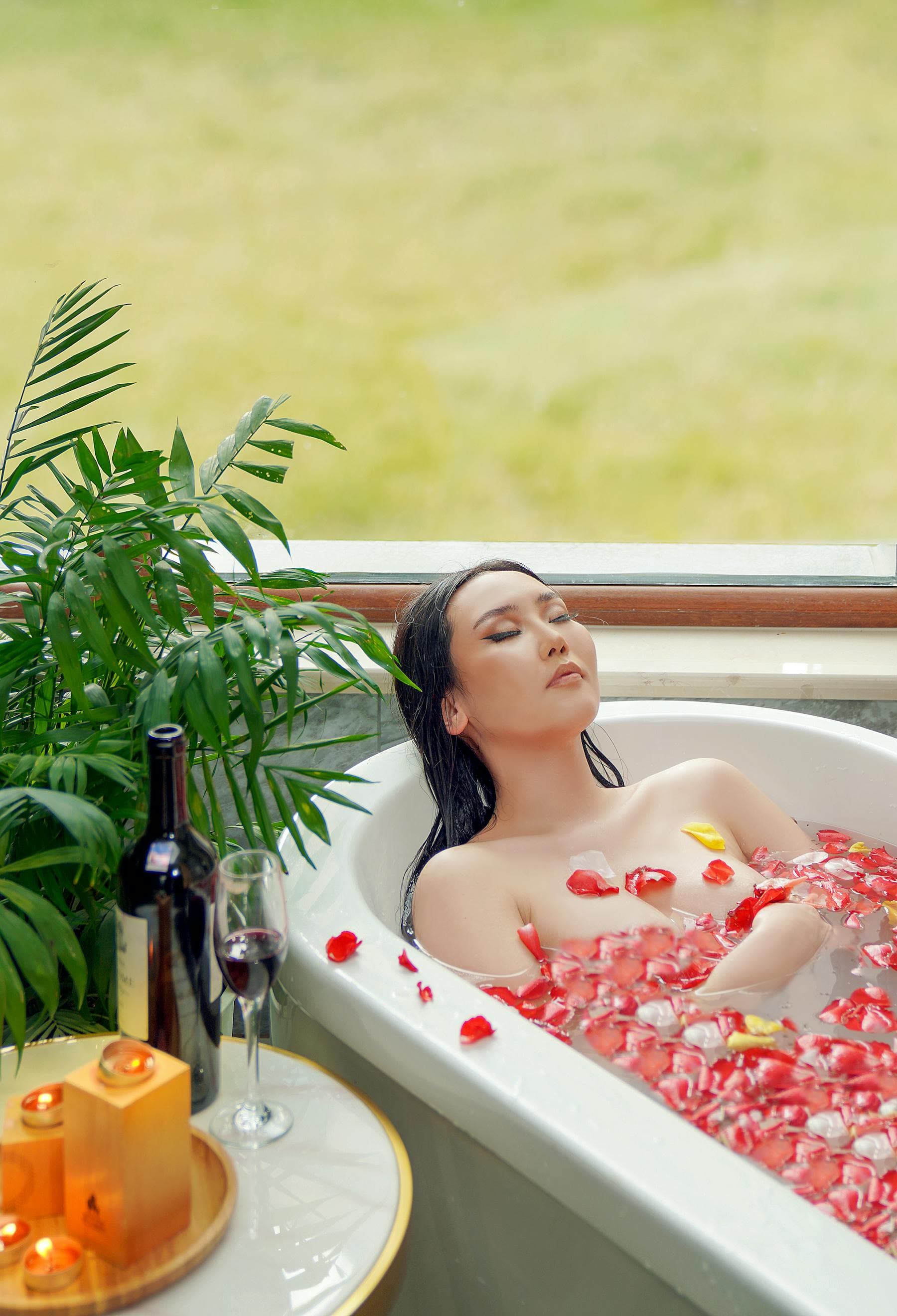 향초와 생화로 장식된 고요한 스파 욕조 — 베트남 전통 허브 목욕에서 영감을 받은 깊은 휴식과 회복의 풍경. 호이안 강변 호텔이자 웰니스 스파인 Nghê Prana에서.