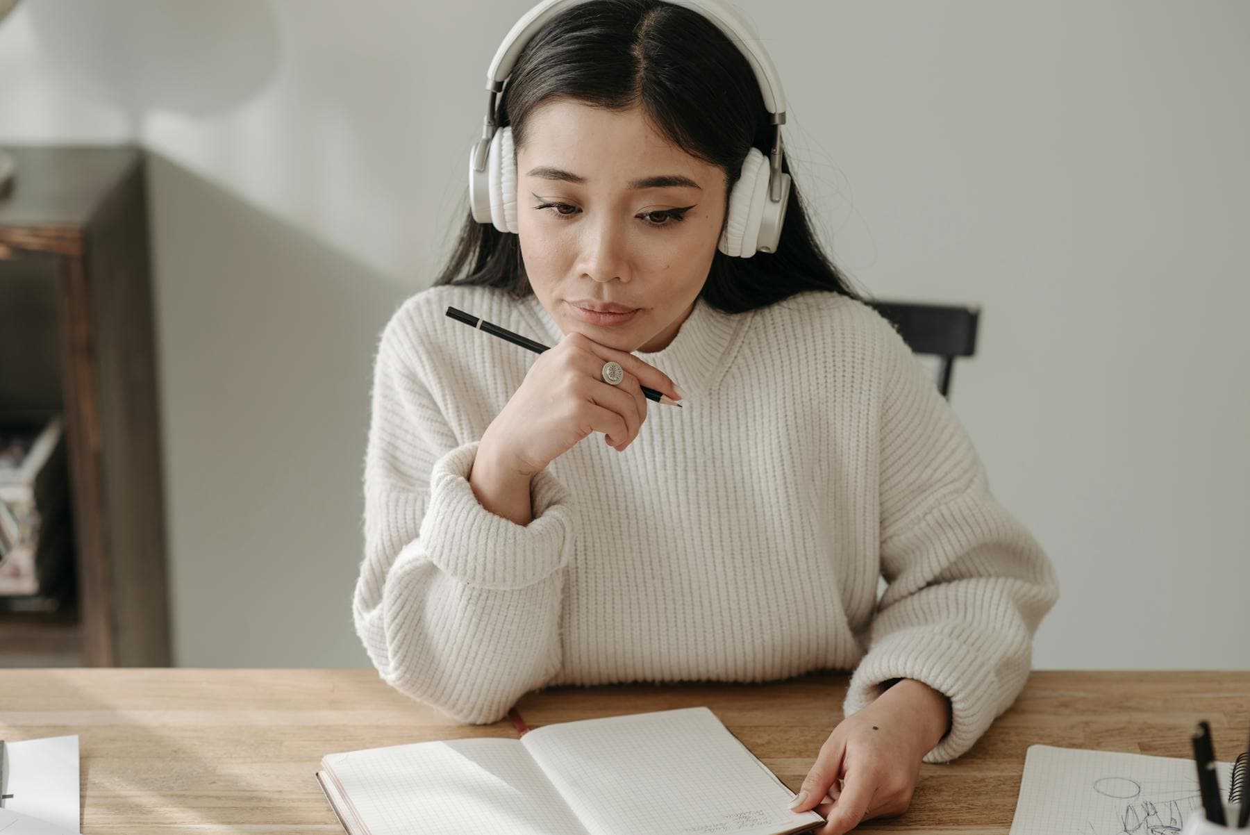 헤드폰을 끼고 노트에 쓰는 젊은 여성 — 호이안 여행 전 베트남어 표현 학습